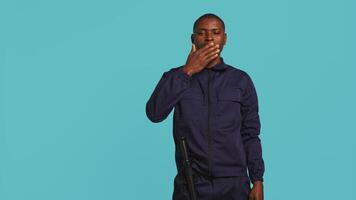 Tired security guard yawning while being tasked with preventing criminal activity and detaining suspects. Portrait of bodyguard showing exhaustion signs during night shift, studio background, camera B video