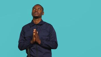 Portrait of security guard waiting for miracle, putting hands together while overseeing premises. Private law enforcement worker looking to sky, praying, studio backdrop, camera A video