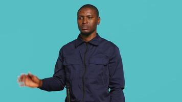 Upbeat security guard greeting people, preventing criminal activity and detaining suspects performing crimes. Portrait of jolly bodyguard waving hand towards visitors, studio background, camera A video
