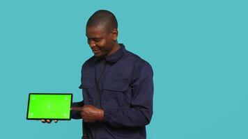 Portrait of happy security staff member showing isolated screen tablet. Joyous patrolling agent maintains secure environment, showcasing chroma key device, studio background, camera A video