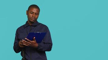 Security guard holding clipboard, taking notes, receiving orders during protection job shift. Portrait of bodyguard using pen to write informations received, studio background, camera A video