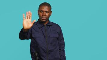 Security guard doing stop sign gesturing, being tasked with preventing criminal activity and detaining suspects. Portrait of stern bodyguard showing halt hand gesture, studio background, camera A video