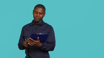 Portrait of security guard holding clipboard, taking notes while overseeing premises. Private law enforcement worker using pen to write down orders received, studio backdrop, camera A video