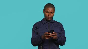 Security guard using smartphone, taking break during protection job shift. Portrait of bodyguard texting friends at work using mobile phone, isolated over studio background, camera A video