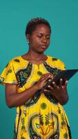 Vertical Happy positive adult navigating on online webpages in studio, using portable gadget to browse things on internet connection. Woman in traditional ethnic attire poses against background. Camera B. video