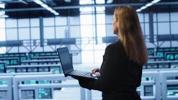 Technician doing yearly maintenance checkup using laptop to prolong data center hardware life span. IT specialist in server hub monitoring server infrastructure using notebook, camera A video