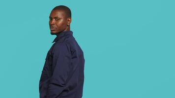 Portrait of security guard overseeing premises to prevent intrusion hearing suspect sounds, turning around. Private law enforcement worker standing isolated with back against studio backdrop, camera A video