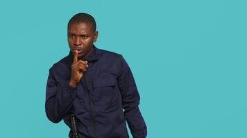 Portrait of security guard doing shush sign gesturing with finger to intruder while overseeing premises. Private law enforcement worker urging people to keep quiet, studio backdrop, camera A video