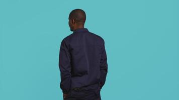 Security guard turning around after hearing suspect sounds during surveillance shift, ensuring protection. Portrait of man in uniform standing isolated with back against studio background, camera B video