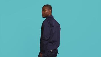 Portrait of security guard overseeing premises to prevent intrusion hearing suspect sounds, turning around. Private law enforcement worker standing isolated with back against studio backdrop, camera B video