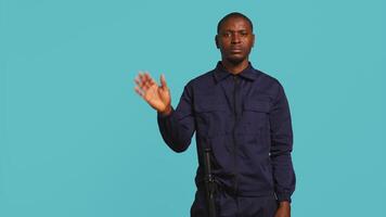 Upbeat security guard greeting people, preventing criminal activity and detaining suspects performing crimes. Portrait of jolly bodyguard waving hand towards visitors, studio background, camera B video