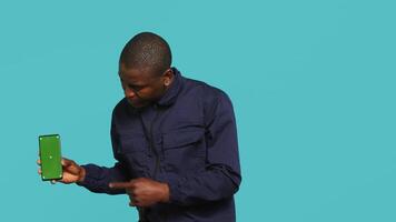 porträtt av säkerhet ombud presenter attrapp telefon och säkring tilldelad posta, studio bakgrund. väktare som visar grön skärm smartphone medan hantering säkerhet överträdelser video