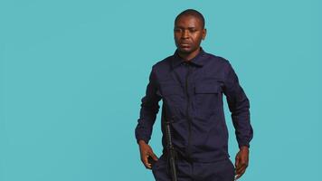 Portrait of security agent securing assigned post, turning on flashlight, studio background. African american guardian prepared to handle security breaches, using lantern device, camera B video