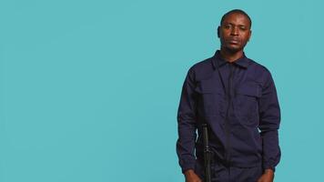 Portrait of security staff member tasked with evicting trespassers, pretending to shoot gun. Patrolling agent maintains secure environment, doing pistol fingers gesturing, studio background, camera B video