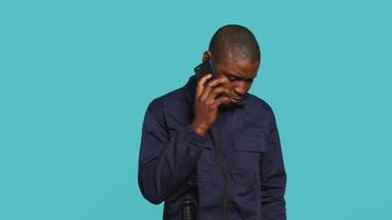 Portrait of security guard at work using phone to make call to friends while overseeing premises. Private law enforcement worker in telephone call with mates, studio backdrop, camera A video
