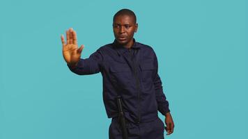 Portrait of security guard doing stop sign gesturing to intruder while overseeing premises. Private law enforcement worker showing halt hand gesture to trespasser, studio backdrop, camera B video