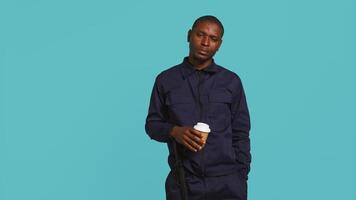 Portrait of security agent uses coffee cup to remain energized while securing assigned post, studio background. Guardian consuming caffeinated beverage to be able to handle security breaches, camera B video