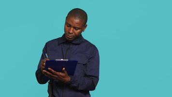 Portrait of security agent holding clipboard, taking notes, receiving orders to secure assigned post, studio background. Guardian maintains logs of observations, handling security breaches, camera A video