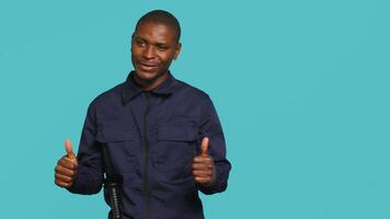 Portrait of joyous security guard doing thumbs up sign gesturing with finger while overseeing premises. Private law enforcement worker doing positive hand gesture, studio backdrop, camera A video