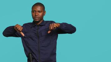 Portrait of security guard doing thumbs down sign gesturing, denying access while overseeing premises. Private law enforcement worker doing negative hand gesture, studio backdrop, camera A video