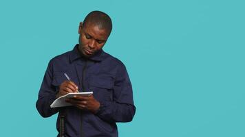 Security guard with notepad taking notes, receiving orders about suspects to look out. Portrait of bodyguard using pen, documenting layout location in need of protection, studio background, camera A video