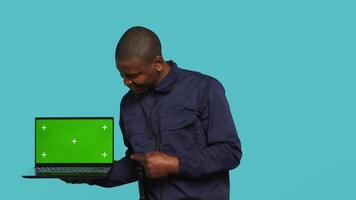 Portrait of happy security guard at work showcasing green screen laptop while overseeing premises. Cheerful private law enforcement worker presenting chroma key notebook, studio backdrop, camera A video