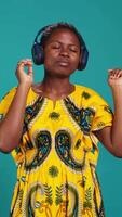 Vertical Carefree relaxed woman listening to music and dancing in the studio, having fun with a new groovy playlist. Happy optimistic person enjoys radio songs on her audio headset. Camera B. video