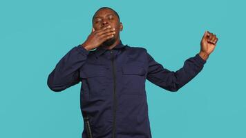 Tired security guard yawning while being tasked with preventing criminal activity and detaining suspects. Portrait of bodyguard showing exhaustion signs during night shift, studio background, camera A video