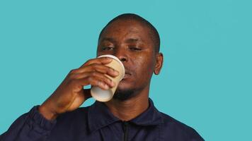huvudskott porträtt av säkerhet ombud dricka kaffe till sluta gapande medan säkring tilldelad posta, studio bakgrund. stänga upp skott av väktare förbrukande koffeinhaltig dryck, kamera en video