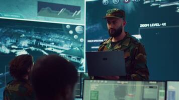 Special operations soldier allocating resources to different units based on mission needs, examines strategic data on a big screen in military control center. Marine corps troops. Camera A. video