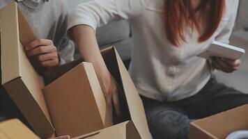 Young couple relaxing sitting on the sofa using the computer laptop around cardboard boxes, very happy moving to a new house. video