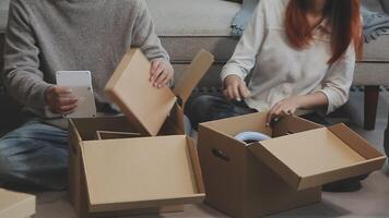 Young couple relaxing sitting on the sofa using the computer laptop around cardboard boxes, very happy moving to a new house. video