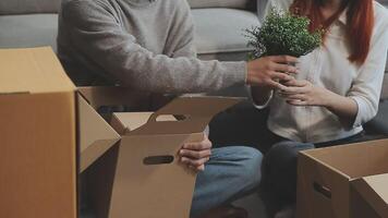 Young couple relaxing sitting on the sofa using the computer laptop around cardboard boxes, very happy moving to a new house. video