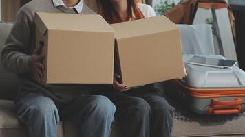 Young couple relaxing sitting on the sofa using the computer laptop around cardboard boxes, very happy moving to a new house. video