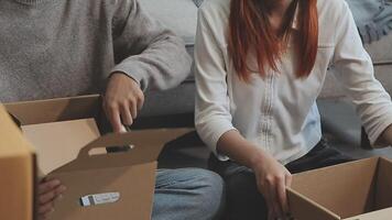 Young couple relaxing sitting on the sofa using the computer laptop around cardboard boxes, very happy moving to a new house. video