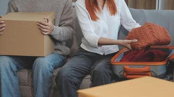 Young couple relaxing sitting on the sofa using the computer laptop around cardboard boxes, very happy moving to a new house. video