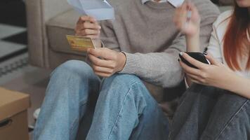 Young couple relaxing sitting on the sofa using the computer laptop around cardboard boxes, very happy moving to a new house. video