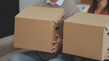 Young couple relaxing sitting on the sofa using the computer laptop around cardboard boxes, very happy moving to a new house. video