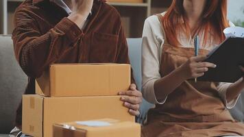 Young couple relaxing sitting on the sofa using the computer laptop around cardboard boxes, very happy moving to a new house. video