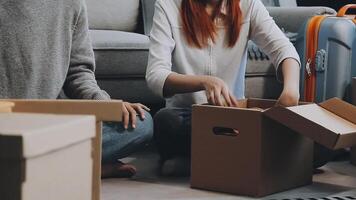 Young couple relaxing sitting on the sofa using the computer laptop around cardboard boxes, very happy moving to a new house. video