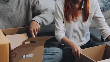 Young couple relaxing sitting on the sofa using the computer laptop around cardboard boxes, very happy moving to a new house. video