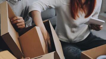 Young couple relaxing sitting on the sofa using the computer laptop around cardboard boxes, very happy moving to a new house. video