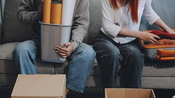 Young couple relaxing sitting on the sofa using the computer laptop around cardboard boxes, very happy moving to a new house. video