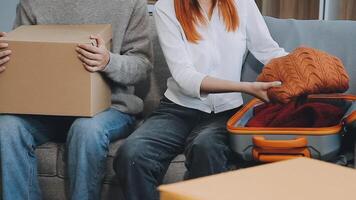 Young couple relaxing sitting on the sofa using the computer laptop around cardboard boxes, very happy moving to a new house. video