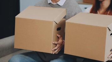 Young couple relaxing sitting on the sofa using the computer laptop around cardboard boxes, very happy moving to a new house. video