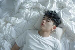 Asian man 20 yo in a white clothes laying down on white bed with white blanket, happily sleeping photo