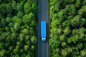Aerial view of a blue transportation truck on an empty road in middle of a green trees forest photo
