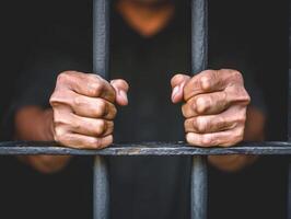 A close-up image of a prisoners clenched fists gripping the bars of a jail cell photo