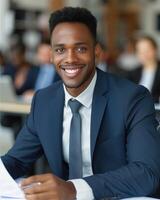 A smiling businessman in a blue suit sits at a desk in an office environment photo