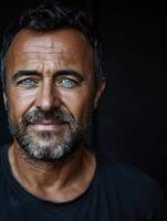 A man with salt-and-pepper beard and piercing blue eyes gazes directly at the camera photo